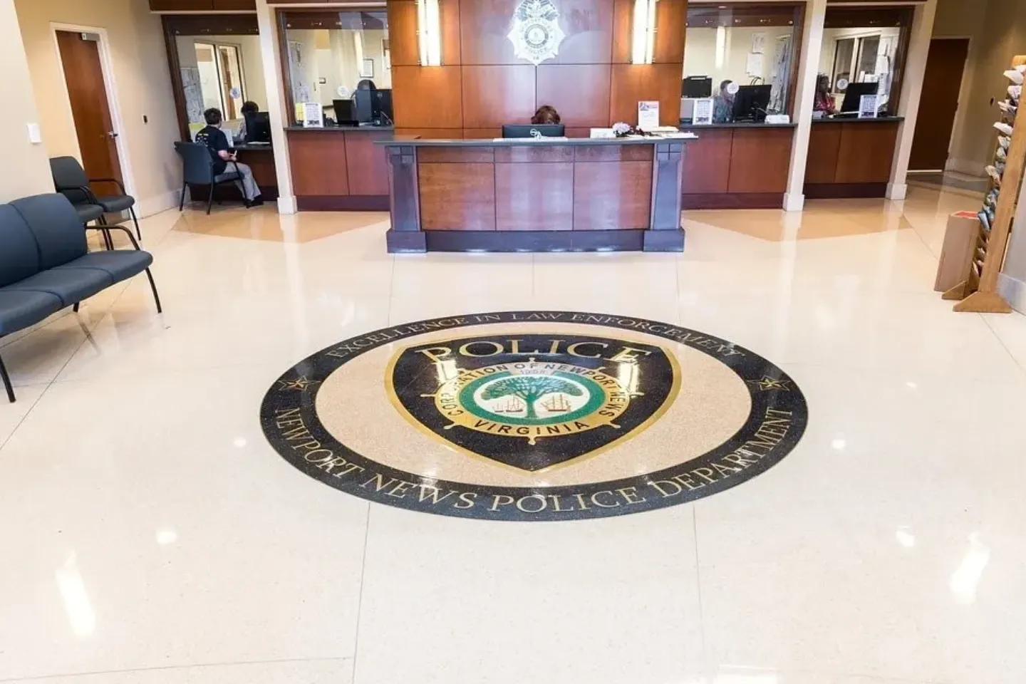 Police department lobby with a circular floor emblem featuring "Newport News Police Department, Virginia." Reception area in the background with staff and counters.