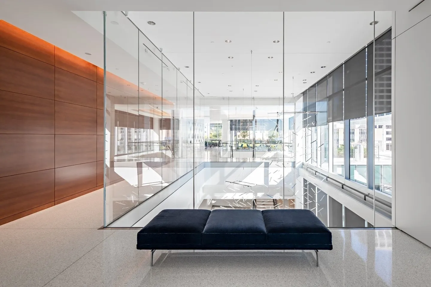 Modern office interior with a black bench in the foreground, large glass walls, and natural light streaming through windows in the background.